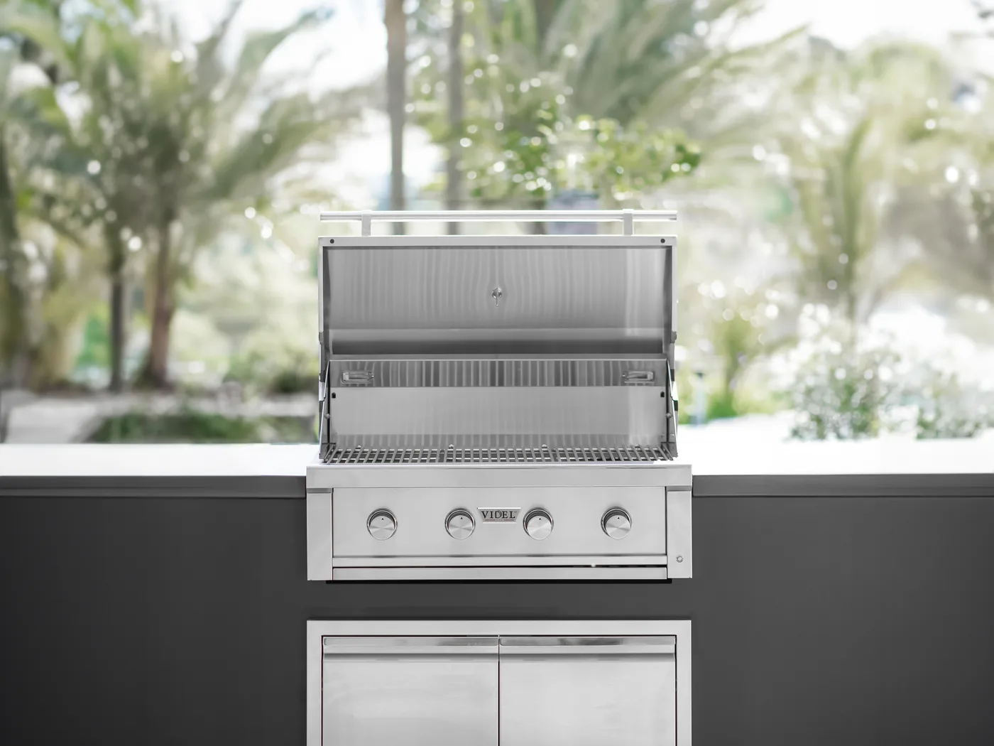 A stainless built-in BBQ set into a finished outdoor kitchen island, with palms behind it